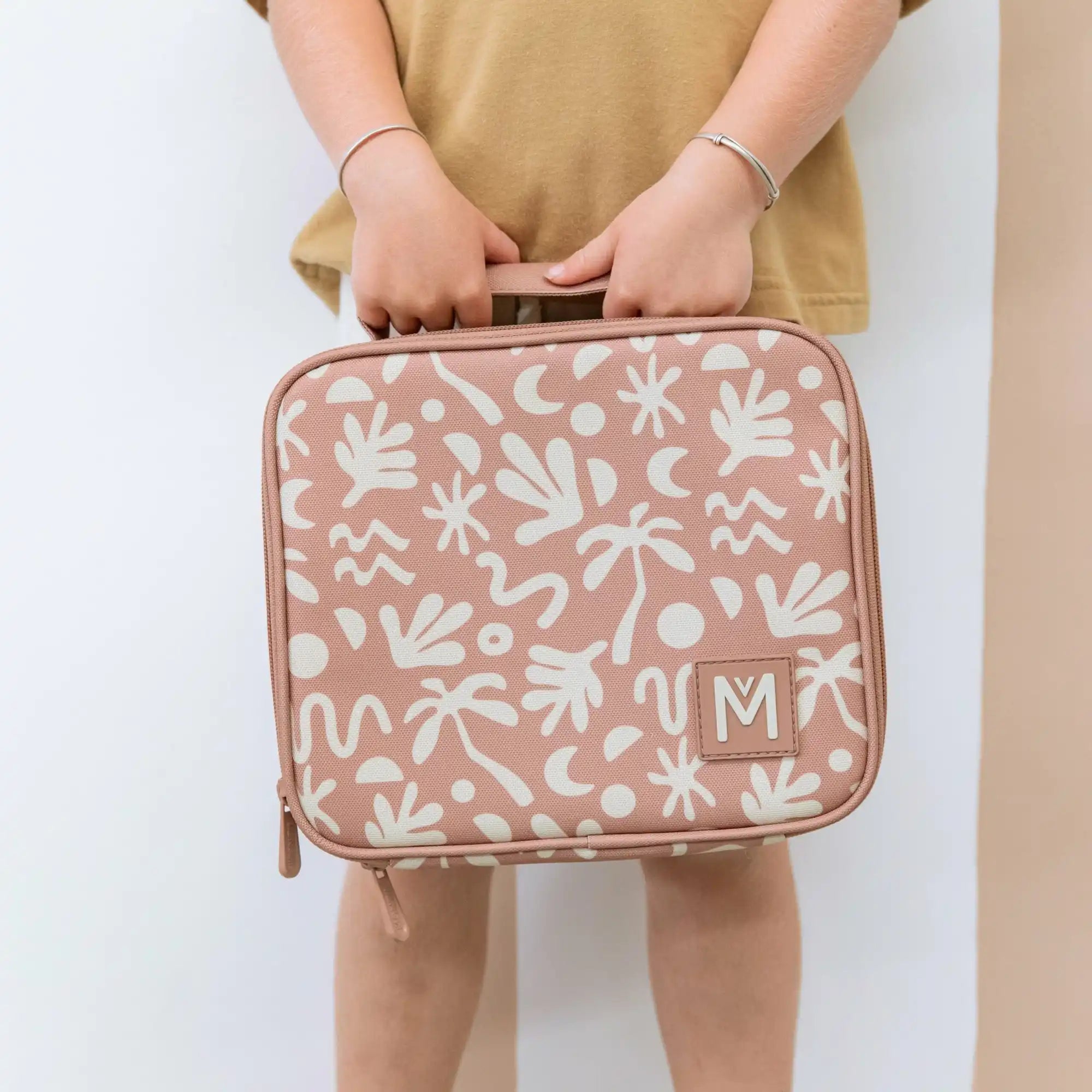 Pink floral patterned lunch box with white botanical designs and a monogrammed ’M’.